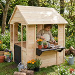 Child playing in a wooden playhouse with gardening tools and plants in a garden setting.